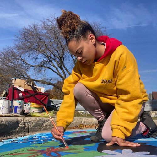 girl painting a storm drain with bright colors